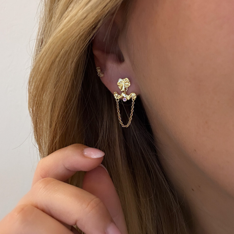Ørering i guld hvor der sidder et aflangt vedhæng på en pink zirconiasten og en kæde der går fra den ene ende til den anden. på selve ørestikken sidder en organisk næsten rund guld plad